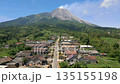 Aerial view of rural village with traditional houses and road leading toward Mount Merapi volcano in Central Java, Indonesia. Scenic landscape showing everyday life near an active volcano. 135155198