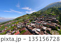 Cinematic FPV flight over rural village on the slopes of Mount Sumbing in Central Java, Indonesia, with green hills, terraced fields and traditional houses under blue sky. 135156728