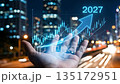 Business growth 2027: Hand holding holographic financial chart with rising arrow. 135172951