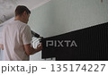 Skilled professional male worker using heat gun to soften adhesive and remove old soundproofing foam panel from interior wall during diy home renovation project, shooting from below, slow motion. 135174227