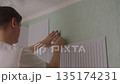Man preparing to applying soundproofing panels to wall, cutting double-sided adhesive tape for home improvement, noise reduction and sound insulation in residential space. 135174231