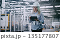 Female Engineer in Hard Hat Checks Production Data on Tablet While Walking Through Automated Factory 135177807