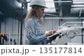 Professional Woman Engineer in Safety Helmet Checking Information on Tablet 135177814