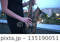 A young woman stands atop a city building, playing saxophone under the stars, her music echoing through the quiet streets of the bustling city center at night. 135190051