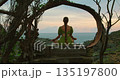Woman in green dress meditates in wooden structure with ocean sunset background in Nusa Penida Bali 135197800