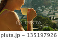 Woman sipping morning cappuccino on terrace with panoramic view of Capri Italy town and coastline 135197926