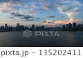 View of central Tokyo from Rainbow Bridge, with buildings and clouds passing by as the sun sets. Time-lapse evening view 135202411