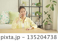 A smiling Japanese woman talking on a smartphone in the living room 135204738