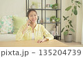 A smiling Japanese woman talking on a smartphone in the living room 135204739