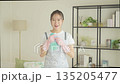 Smiling young Japanese woman holding towels and detergent in the living room, housekeeping 135205477