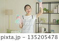 Smiling young Japanese woman holding towels and detergent in the living room, housekeeping 135205478