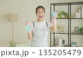 Smiling young Japanese woman holding towels and detergent in the living room, housekeeping 135205479