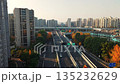 Cars drive on a highway in Hangzhou, China, during the day. Autumn colors highlight the trees. Tall apartment buildings are visible in the background. 135232629