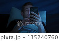 Man lies in bed holding his mobile phone, scrolling social media at night 135240760
