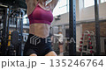 A young beautiful woman in sportswear is training and doing exercises on a horizontal bar with leg raises for the abs in a gym 135246764