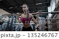 Young beautiful woman in sportswear doing workout and squat exercises for legs with barbell in the gym 135246767