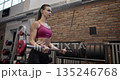 Young beautiful woman in sportswear training and doing exercises for arms and biceps with a small barbell in the gym 135246768