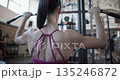 Young beautiful woman in sportswear exercising and doing arm pull-ups on a machine in a gym 135246872