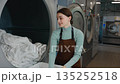 A woman worker is loading various clothes into a washing machine 135252518