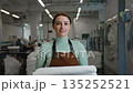 A walking woman worker in an apron holds fresh towels in a laundromat 135252521