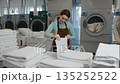 Female worker is carefully folding clean towels in a bustling laundromat 135252522