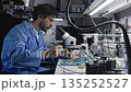 A man soldering technician in a blue lab coat repairs electronics and devices 135252527