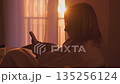 Cozy lifestyle moment with woman using smartphone while resting in warm sun rays. 135256124