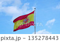 Low angle view of the national flag of Spain waving proudly in the wind against a bright blue sky with white clouds 135278443