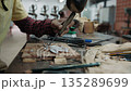 Close up of a carpenter using a chisel and mallet to carefully carve an intricate design into a wooden plank in a workshop, Siem Reap, Cambodia. 135289699