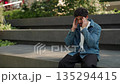 Portrait of tired Latin American man massages temples reducing headache in green park. Hispanic guy deals with migraine attack sitting on parapet in urban district slow motion 135294415