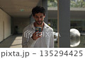 Portrait of curly haired Hispanic man reads message on smartphone as walks on columned passage slow motion. Smiling Latin guy in shirt texts by mobile phone in financial district 135294425