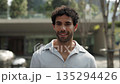 Portrait of attractive Hispanic man in shirt smiles near office building slow motion. Bearded Latin American guy looks at camera with positive vibes against business center in city 135294426
