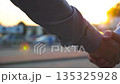 Dolly shot of two confident colleagues meeting and shaking hands at city street on sunset. Successful young businessman greeting each other against the background of cars parking. Close up Slow motion 135325928