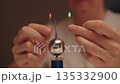 Scientist hands holding two leds near mini tesla coil, observing electrostatic discharge and electrical sparks illuminating light-emitting diodes during physics experiment, close-up, slow motion. 135332900