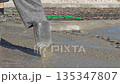 Concrete construction worker spreading wet cement with shovel on building site 135347807