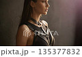 Woman models stylish black leather harness in dramatic studio lighting profile view. Edgy leather harness outfit suits halloween costume or punk fashion concept. Cinematic flare hits harness straps. 135377832