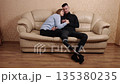 Prosthetic support, Loving bond, Disabled unity. The wife and her husband, with his prosthetic leg, sit together on the couch, holding each other and feeling the happiness and love they share. 135380235