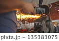 Close up male hands of adult welder cutting steel using electric grinding wheel in workshop. Arms of professional repairman or mechanic worker sawing metal with a circular saw in garage. Slow motion 135383075