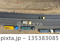 Aerial shot of roller making new asphalt road and trucks standing at roadside. Special machinery repairing roadway in countryside. Drone tracking compactor constructing highway. Top view 135383085