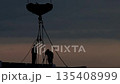 Construction workers silhouettes against evening sky during sunset, crane hook with chains on industrial building site, engineering progress at dusk. 135408999