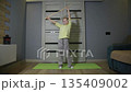 Young Caucasian girl eight years old performing gymnastics exercise with wooden stick indoors home workout activity for healthy child development 135409002