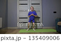 Young Caucasian girl doing home workout performing leg lifts and squats on exercise mat. Child fitness activity for strength and health development at residence. 135409006