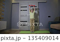 Young caucasian girl age 8 performs fitness exercise with light red dumbbells indoors at home room during daily workout for physical health 135409014