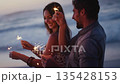 Couple, sparkler and having fun on the beach at sunset while celebrating new years eve with friends. Boyfriend and girlfriend with sparkle to celebrate on a seaside vacation or holiday in Bali 135428153