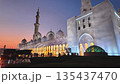 The Sheikh Zayed Grand Mosque is illuminated against blue twilight sky, showcasing its white marble domes and reflective pools in Abu Dhabi, UAE 135437470