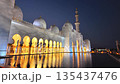 The Sheikh Zayed Grand Mosque is illuminated against blue twilight sky, showcasing its white marble domes and reflective pools in Abu Dhabi, UAE 135437476