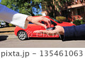 A company manager delivers a red car and hands over the keys to a client, representing car rental service, vehicle delivery, leasing, financing, car sale and ownership transfer. 135461063