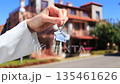 Graceful woman's hand holds silver house keys against the backdrop of a city townhouse. Real estate concept for the sale and purchase of houses and apartments. Real Time video. 135461626