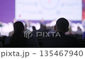 Silhouetted couple watching illuminated screen backlit attendees dark auditorium blurred speakers 135467940