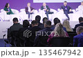 Panelists on stage with audience attentive delegates seated rows purple backdrop white armchairs 135467942